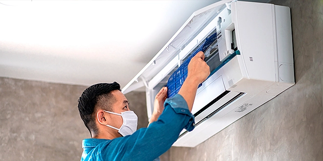 A worker wearing a mask cleaning an AC.