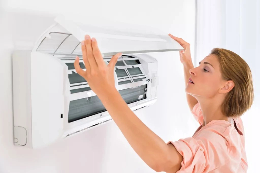 A woman cleaning an indoor AC unit.