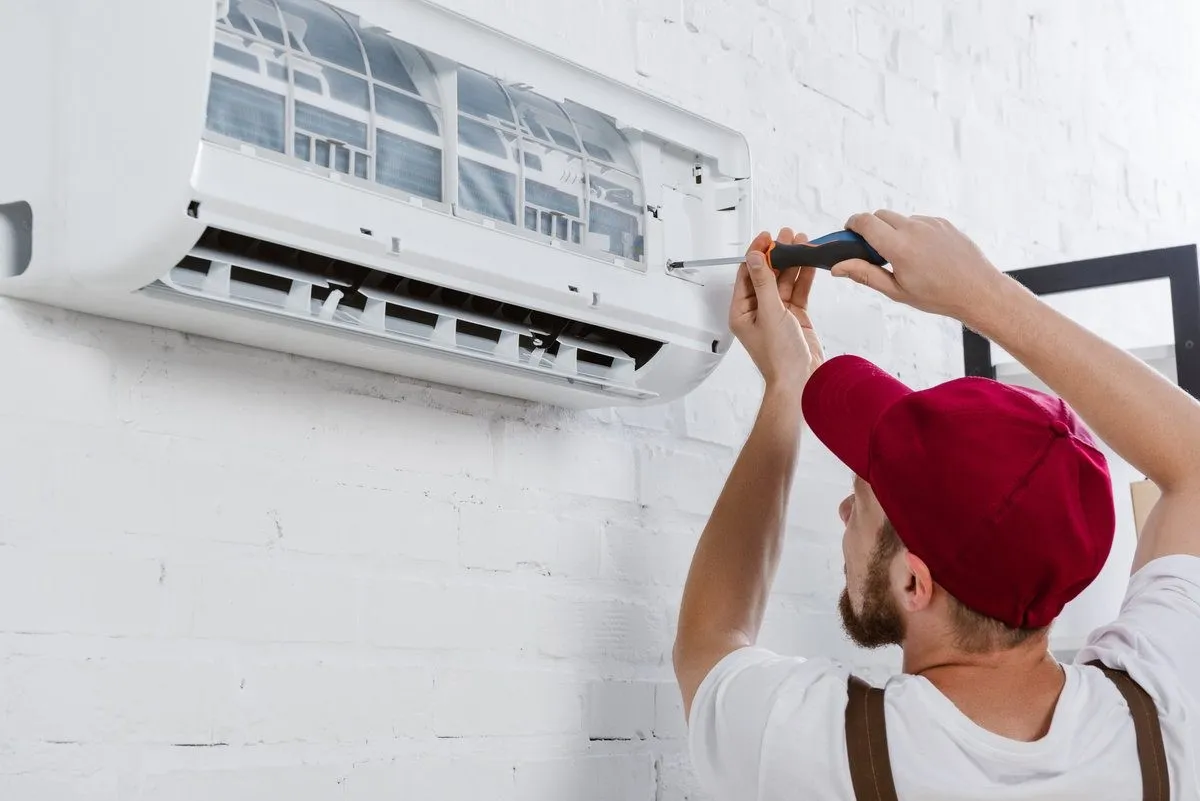 A technician repairing an AC unit with a screwdriver.