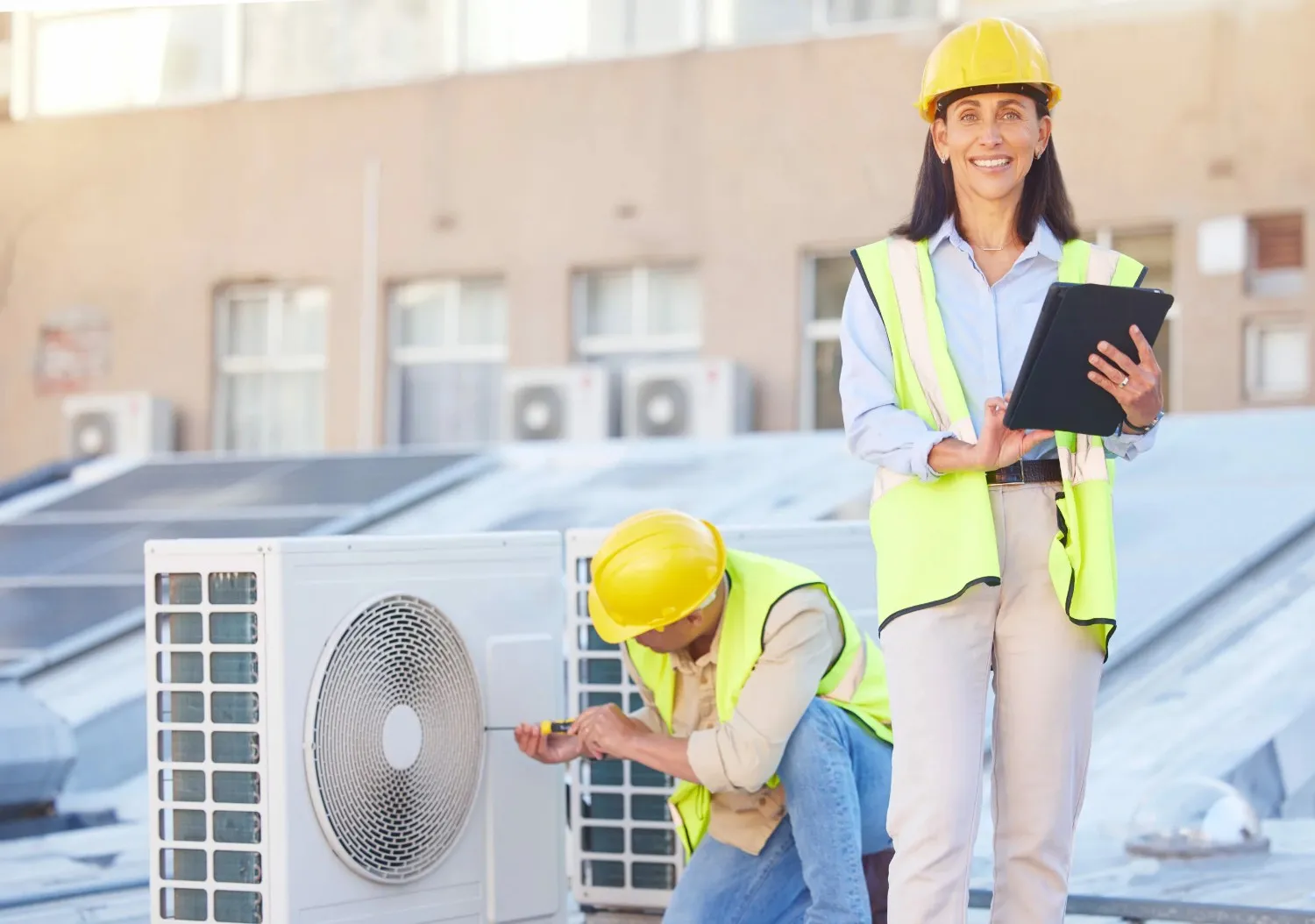 Supervisor watches technician fix rooftop HVAC.