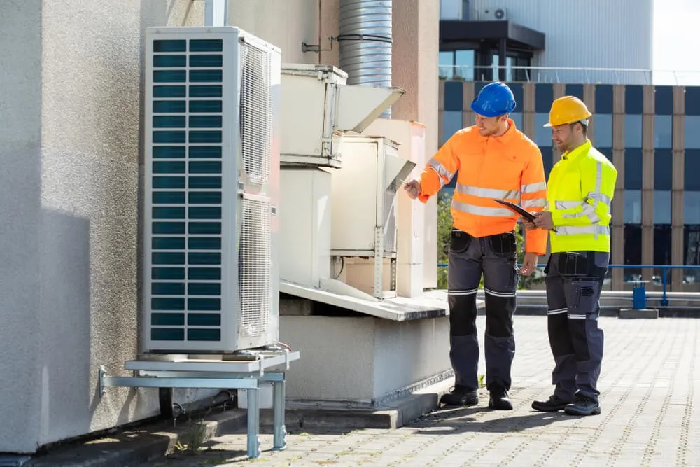 Two workers inspecting outdoor HVAC equipment.