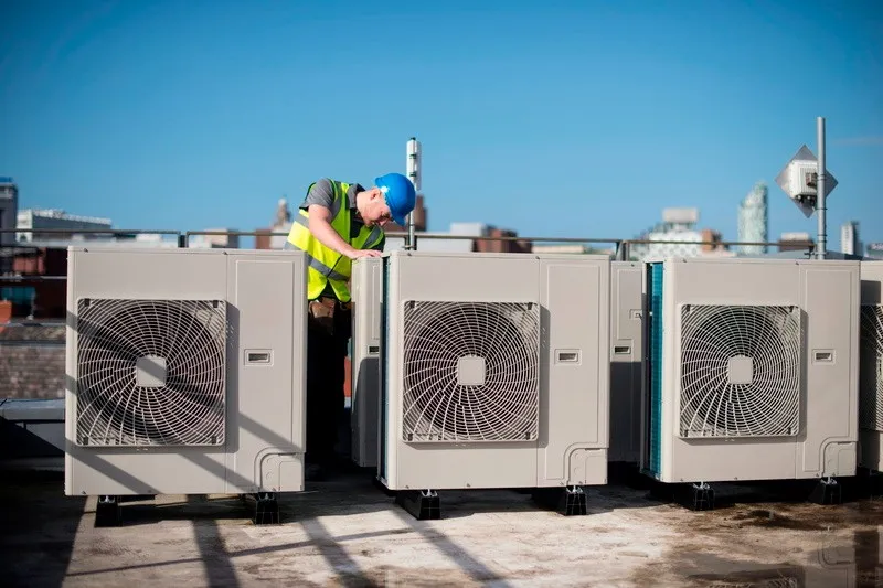 Technician inspecting commercial HVAC units on roof.