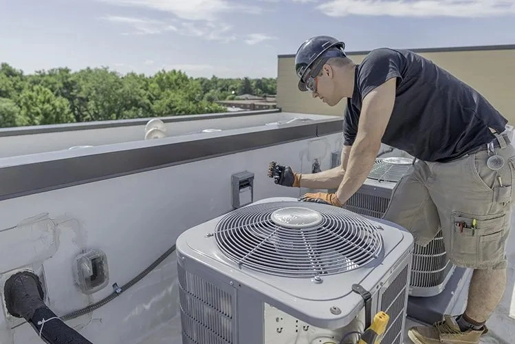 Technician servicing rooftop AC unit on sunny day.