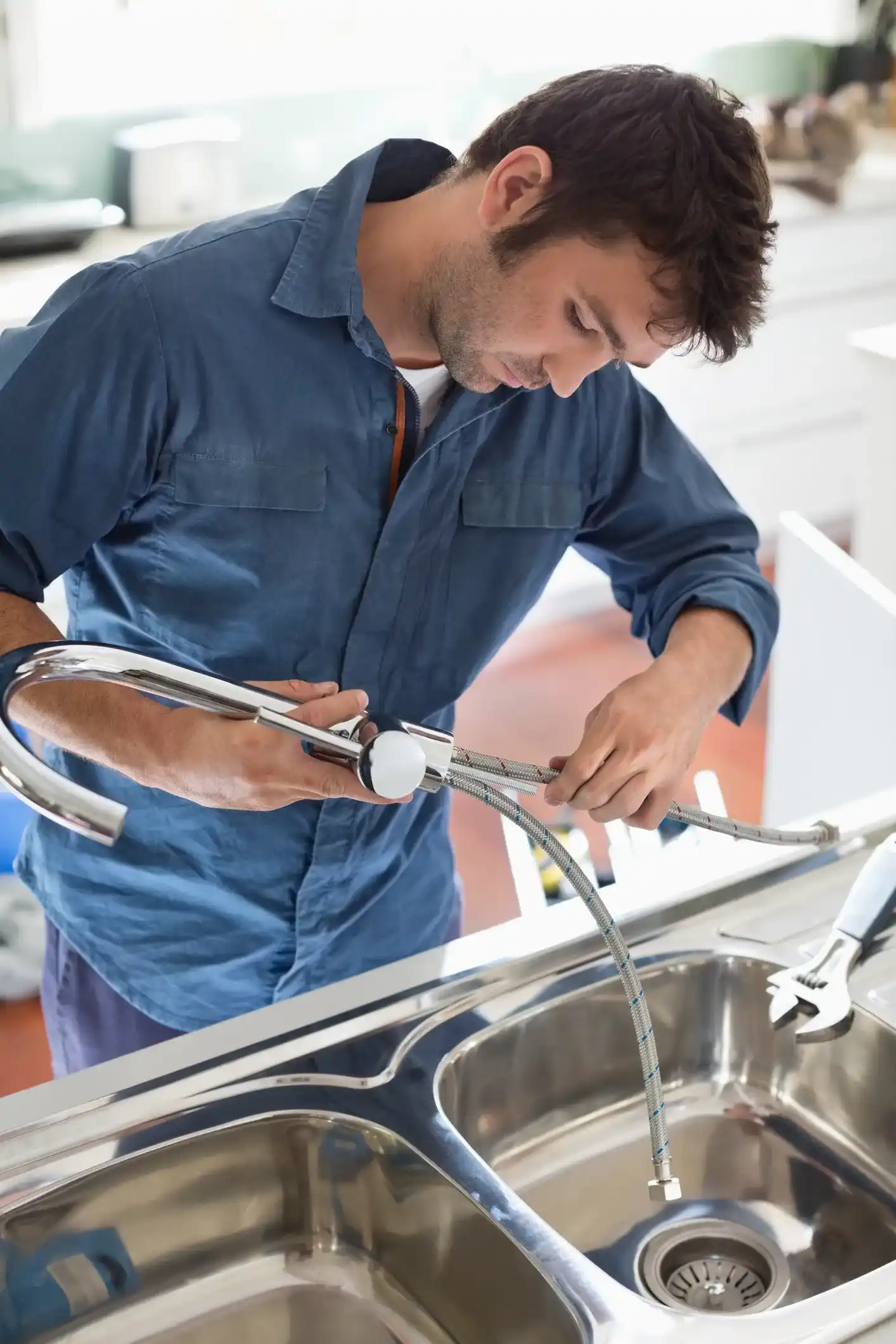 Plumbing contractor preparing a new kitchen faucet with flexible hoses for installation over a double stainless steel sink.