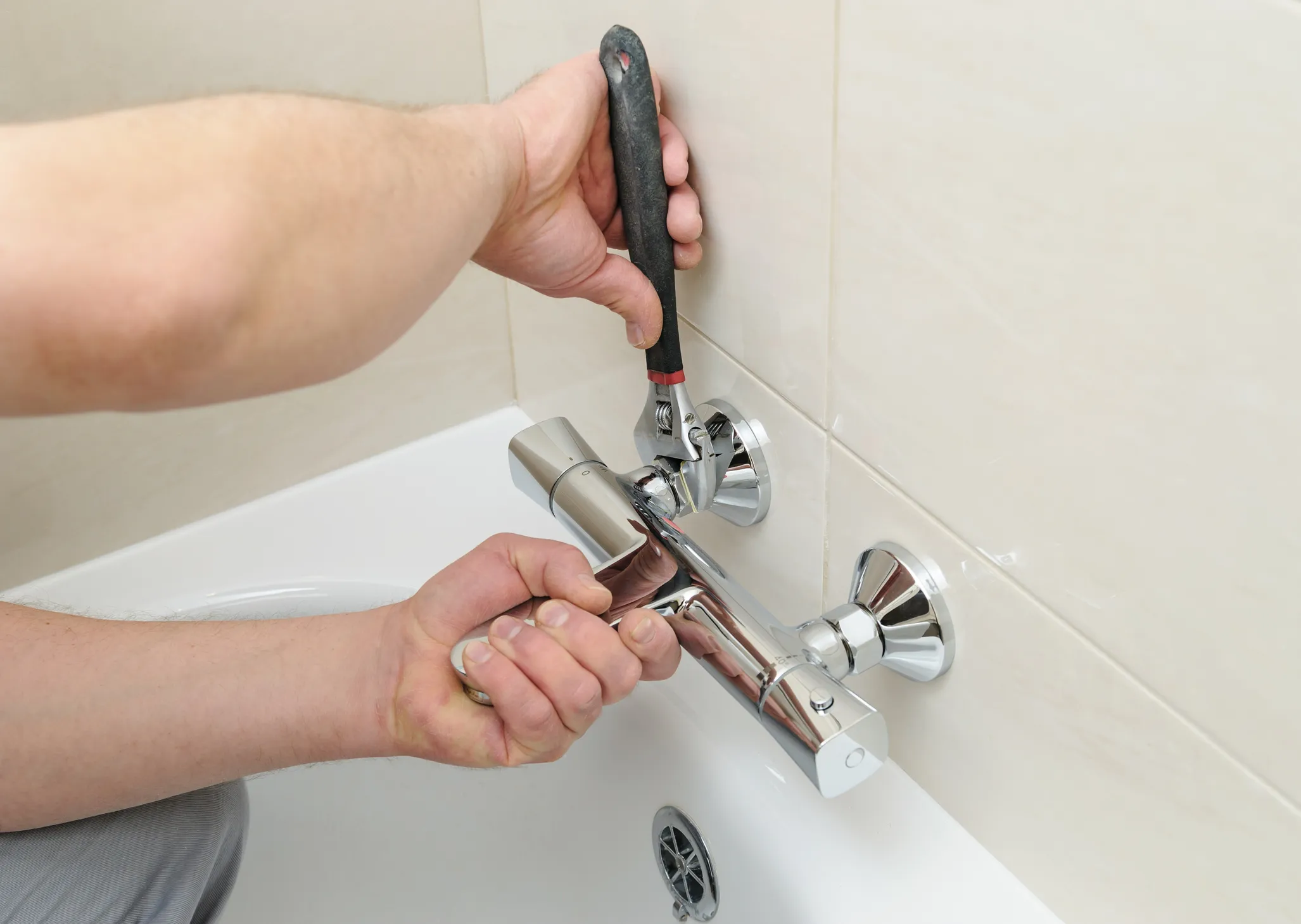 Close-up of a hand using an adjustable wrench to install or repair a shower valve or bathtub mixer faucet.