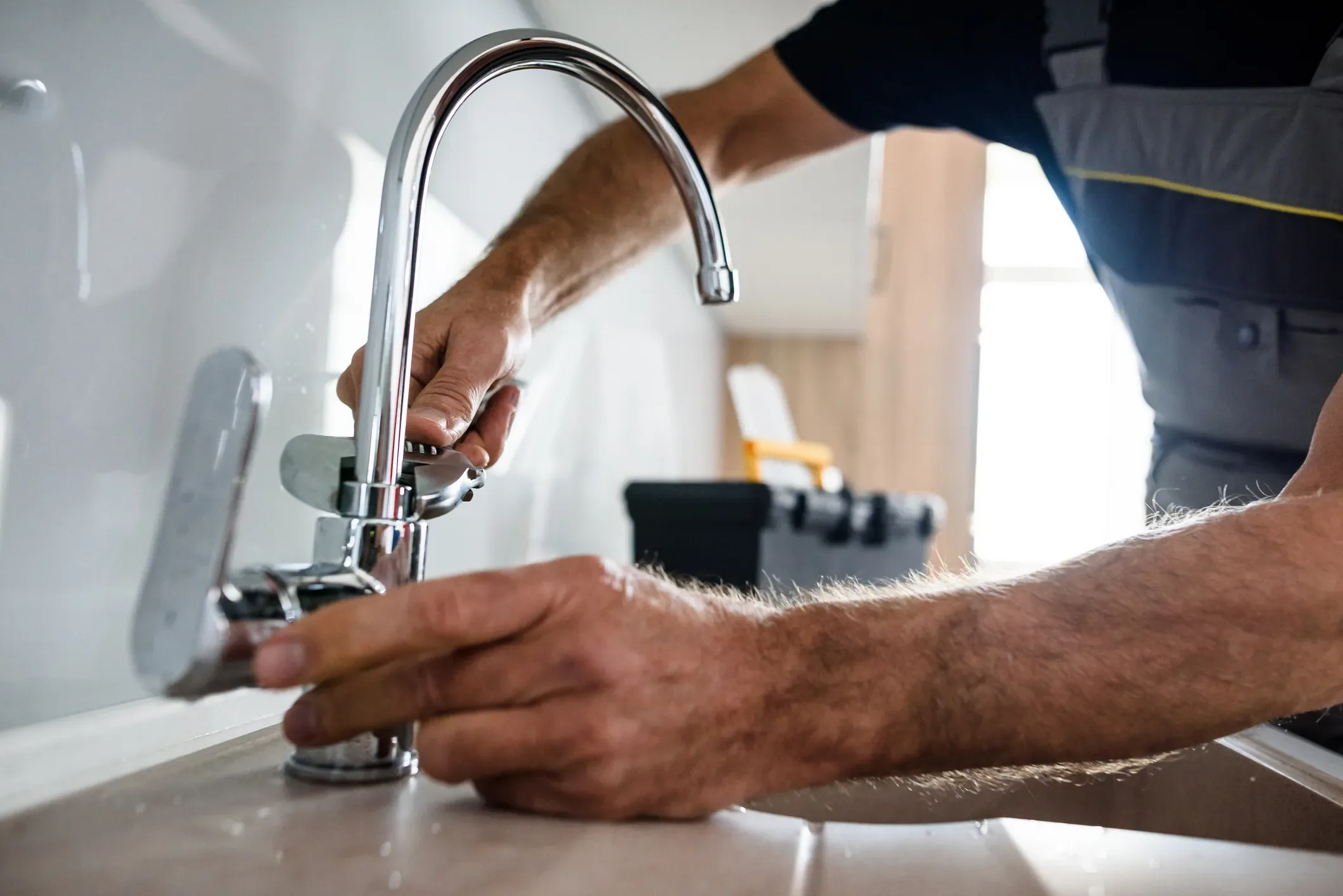 Close-up of a plumber tightening the connection of a chrome kitchen faucet handle on a modern countertop.