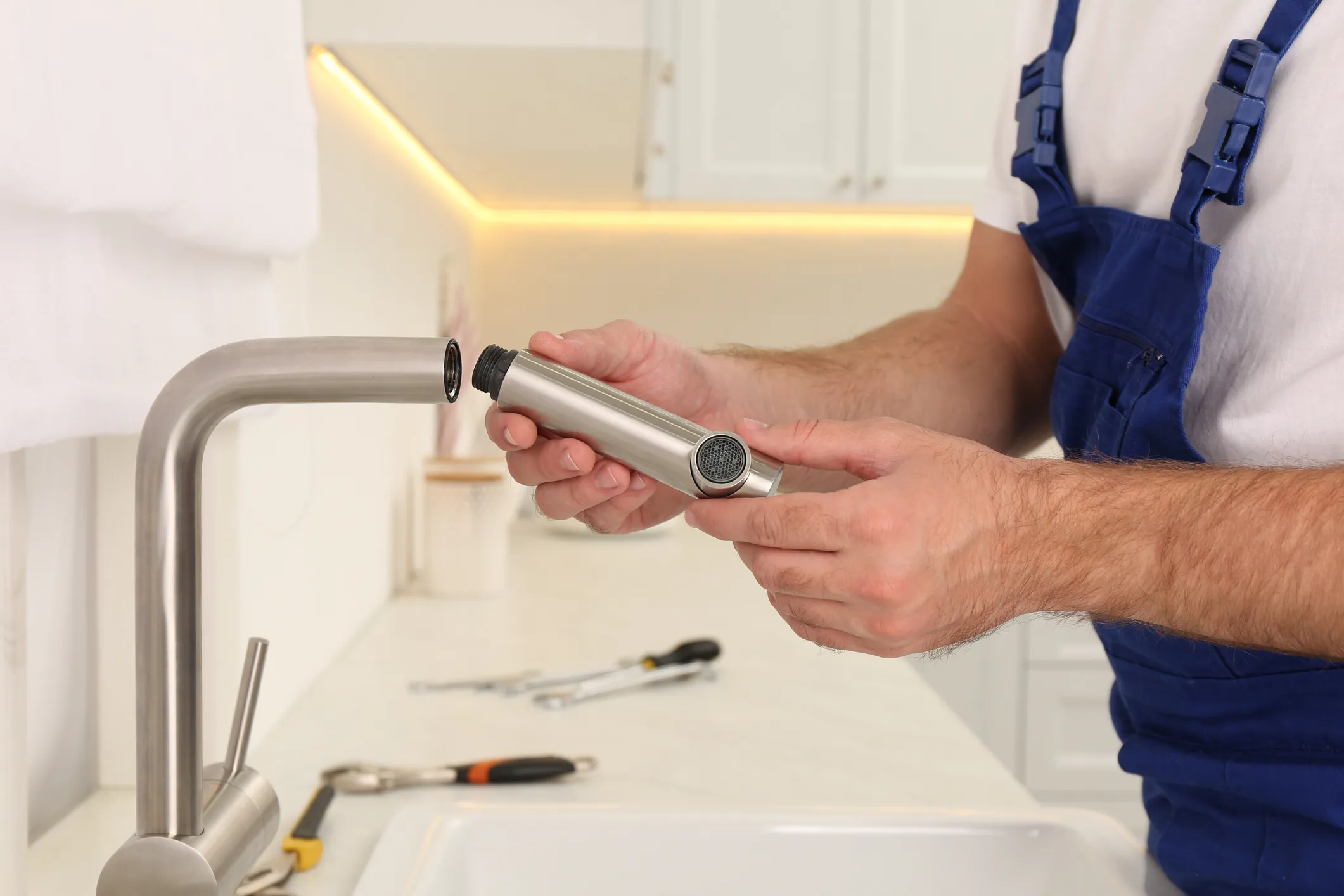 Worker holding the spray head or aerator of a kitchen pull-down faucet while performing repair or maintenance.