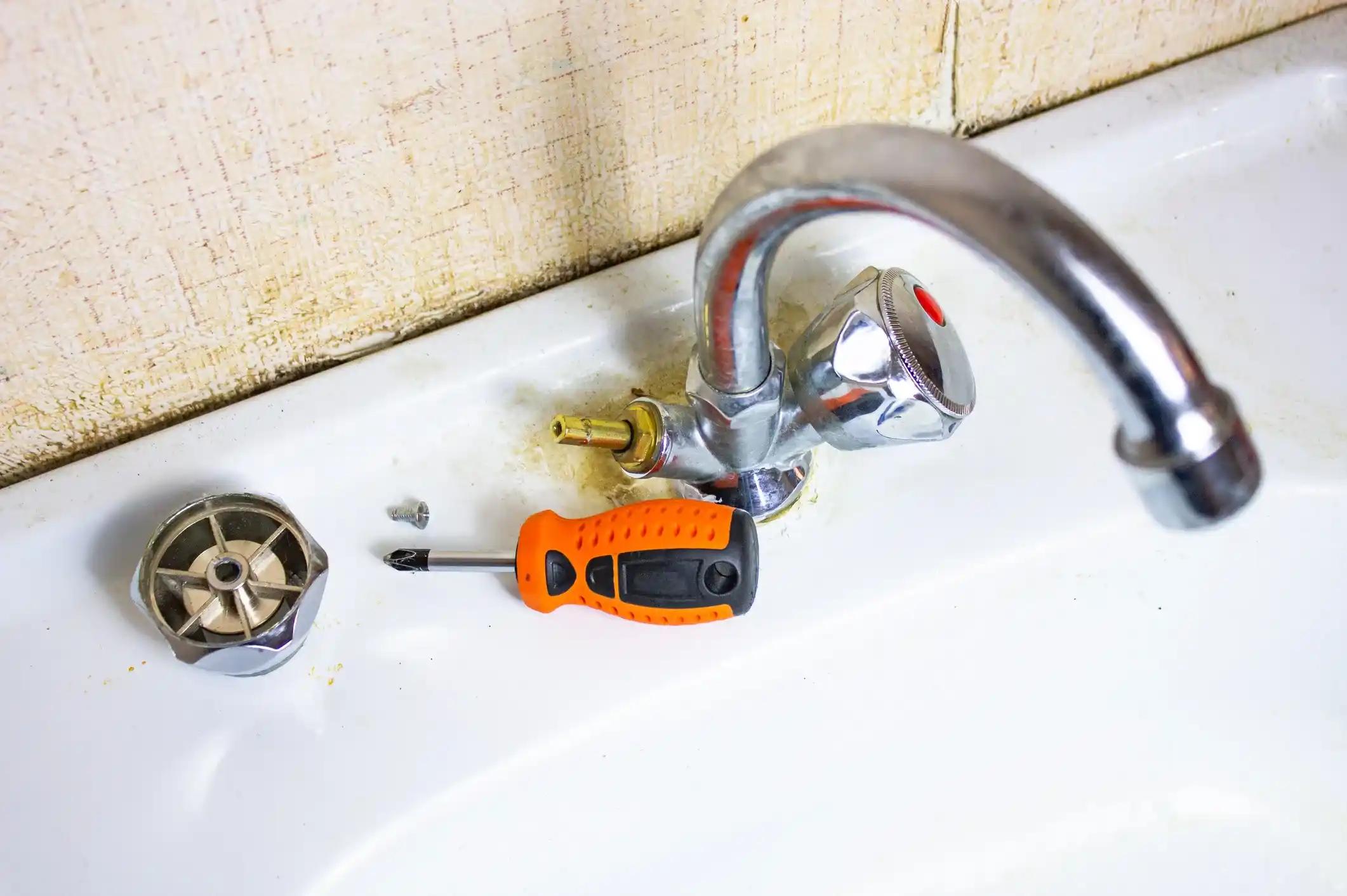 Close-up of a chrome bathroom faucet being repaired, with the valve cartridge and screwdriver visible on the sink basin.