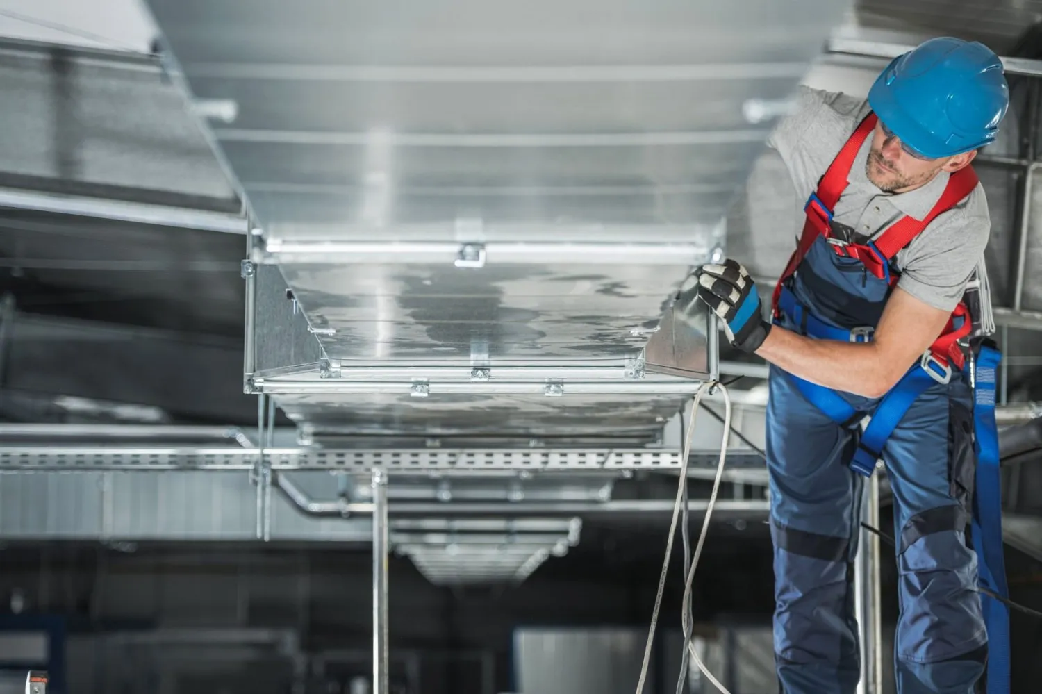 Man installing HVAC ductwork wearing safety gear.