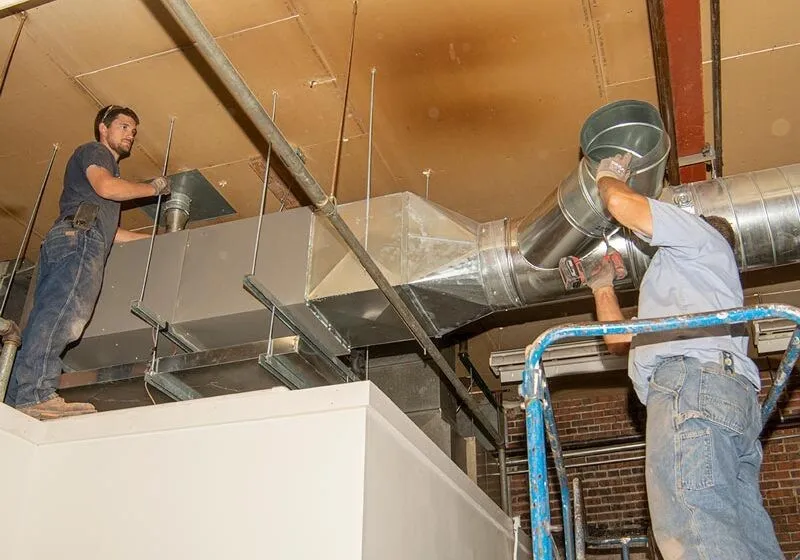 Two technicians installing commercial HVAC ductwork overhead.
