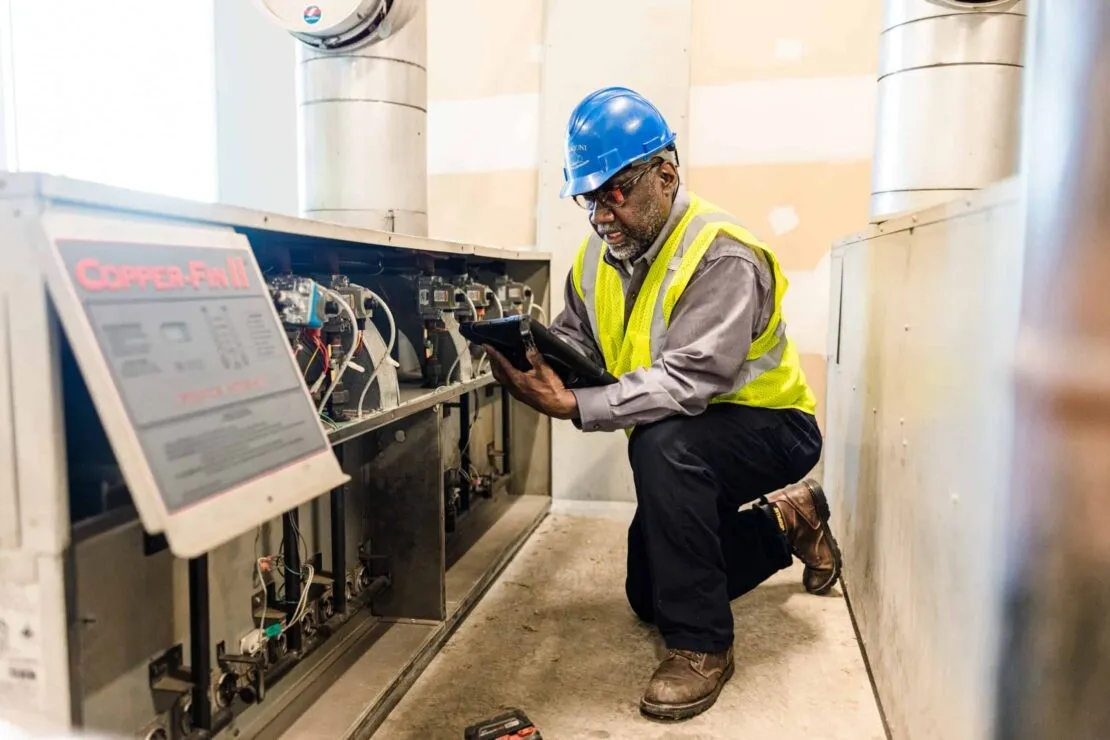 Technician servicing commercial HVAC unit with tablet.
