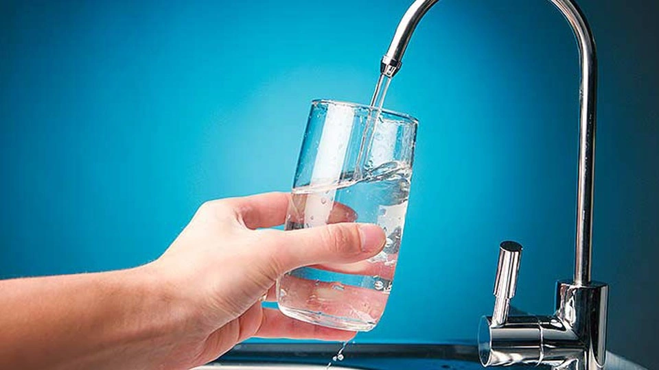 Hand holding glass under running faucet.