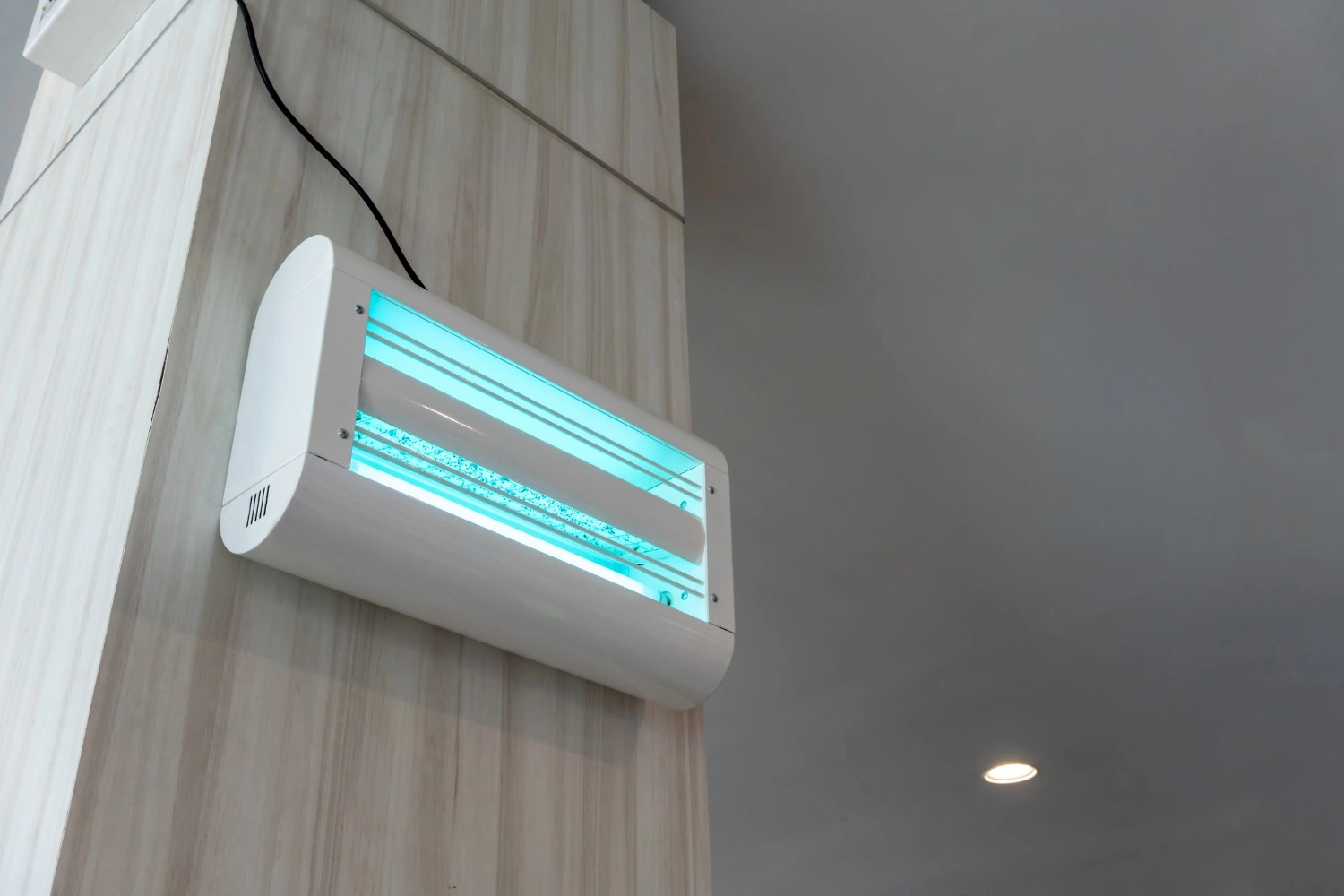 Wall-mounted indoor insect zapper or UV light air sanitizer unit on a wooden panel.