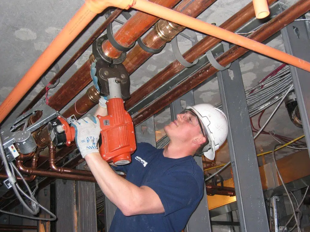 Plumber pressing copper pipe fitting.