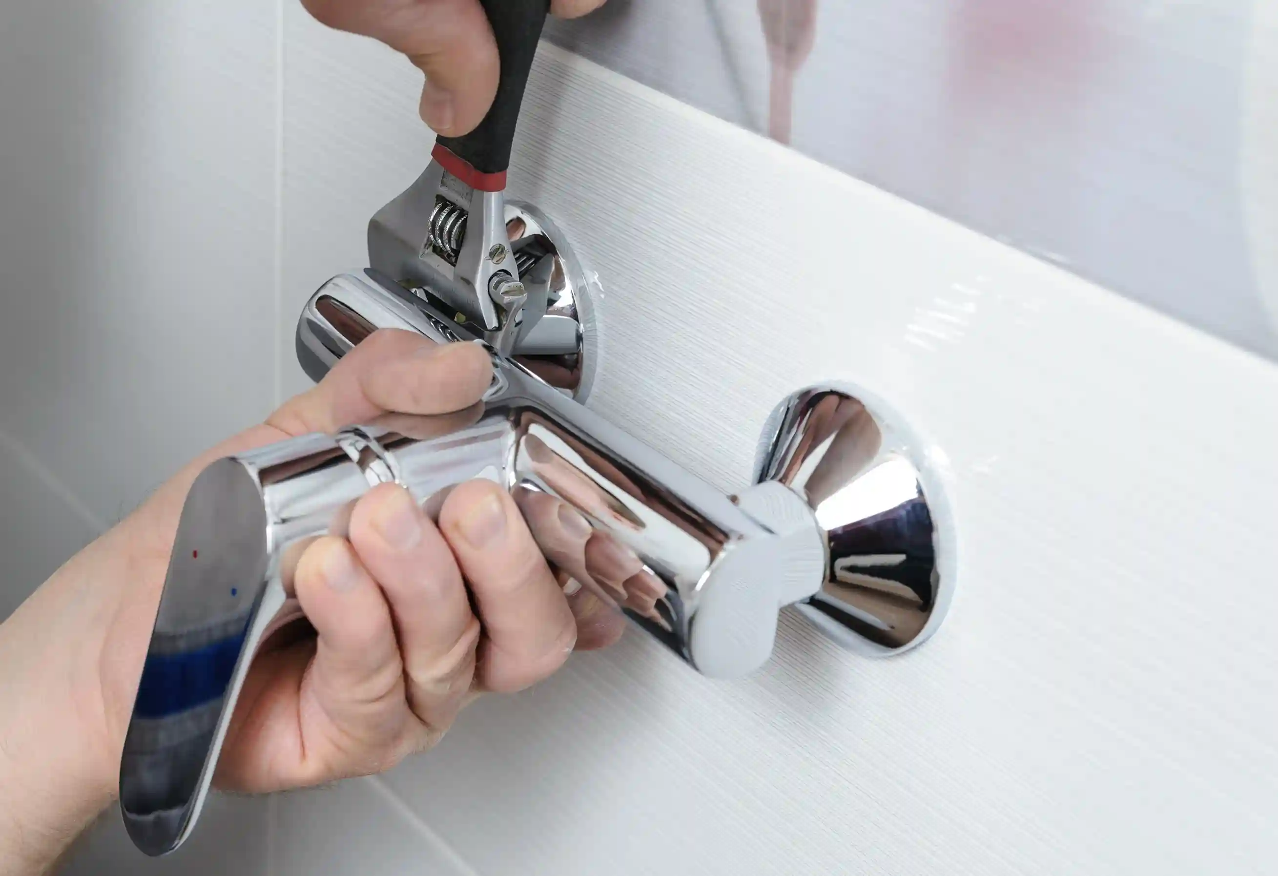 Hands using an adjustable wrench to replace a new chrome shower fixture.