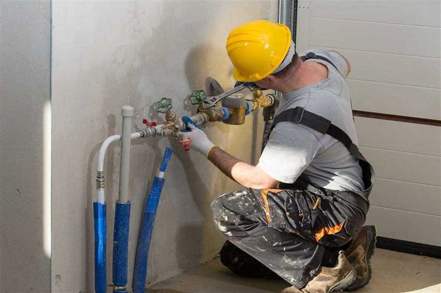 Plumber in hardhat adjusts water meter.