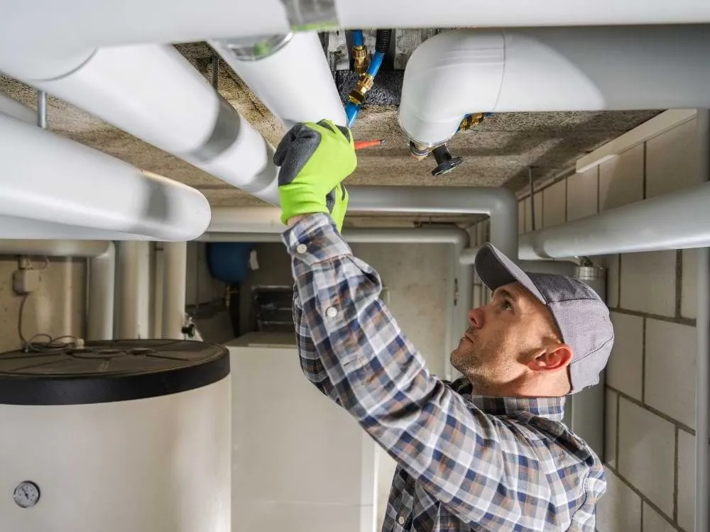 Plumber inspects pipes near large tanks.