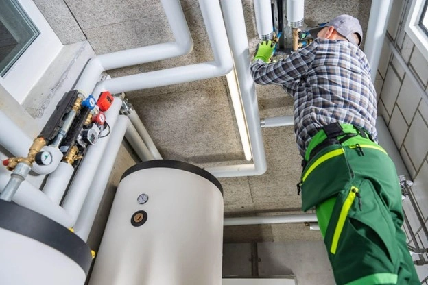 Plumber adjusts pipes above water tanks.