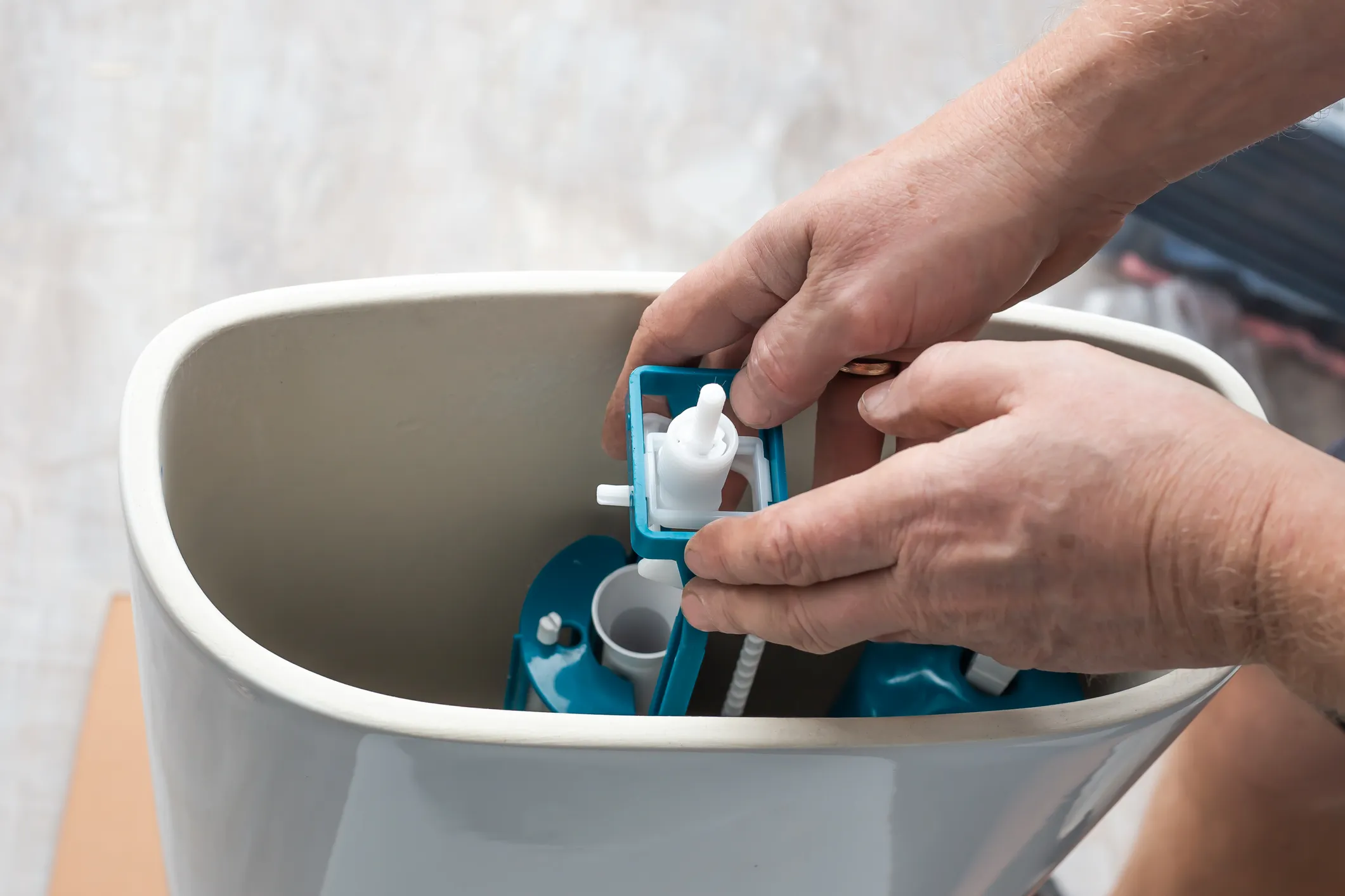 Close-up of a plumber's hands replacing the blue fill valve mechanism inside a toilet tank.