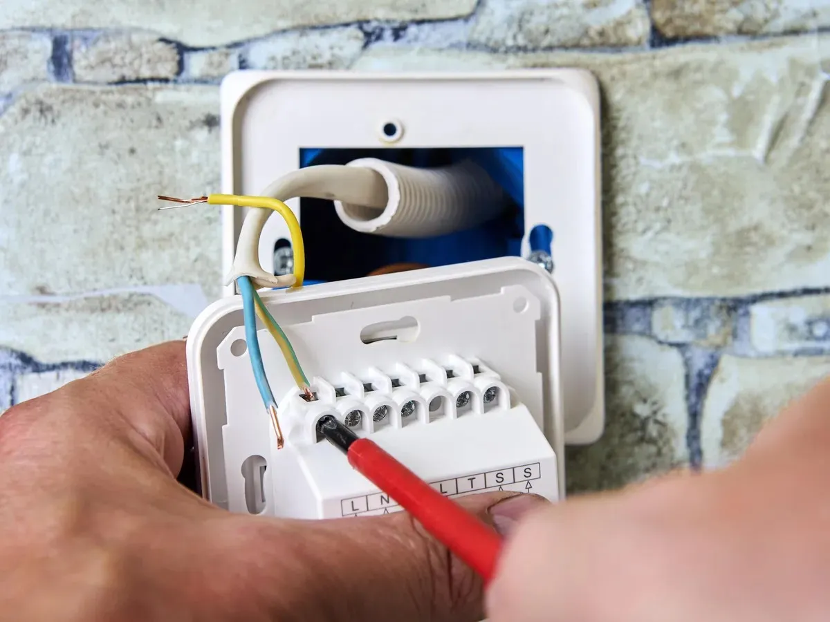 Electrician wiring thermostat terminals with screwdriver.