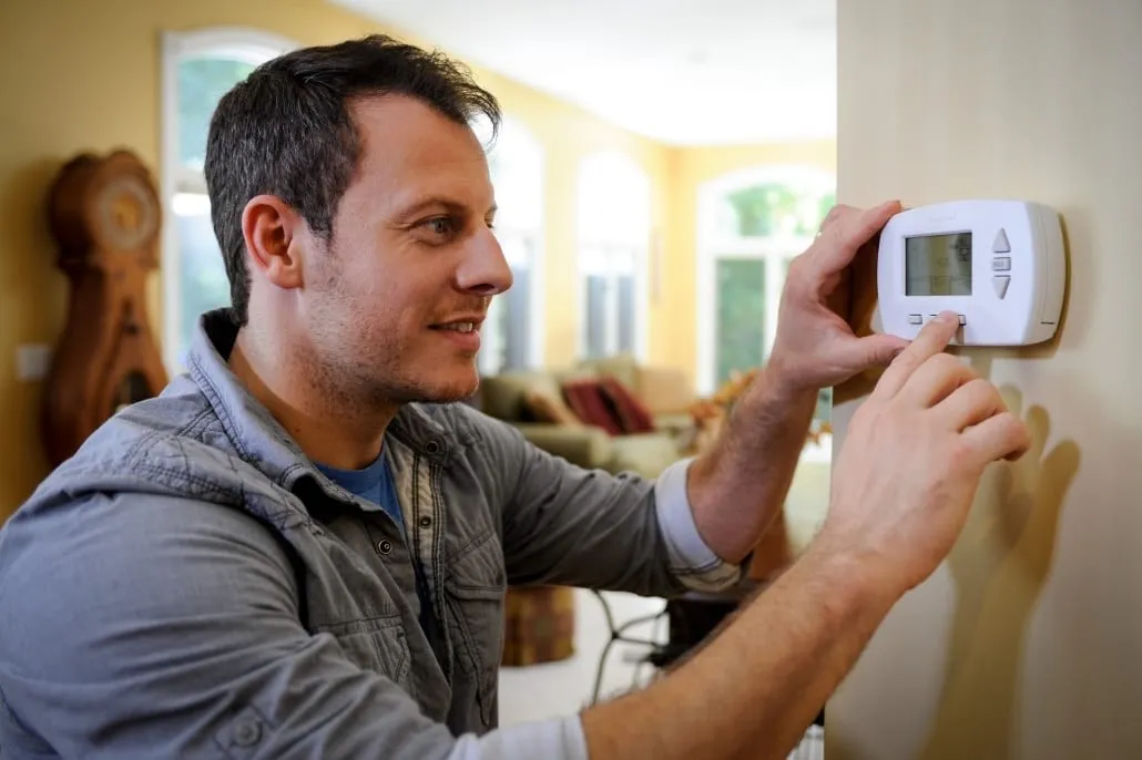 Man adjusts a programmable digital thermostat.