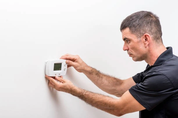 Man mounting a white digital thermostat.
