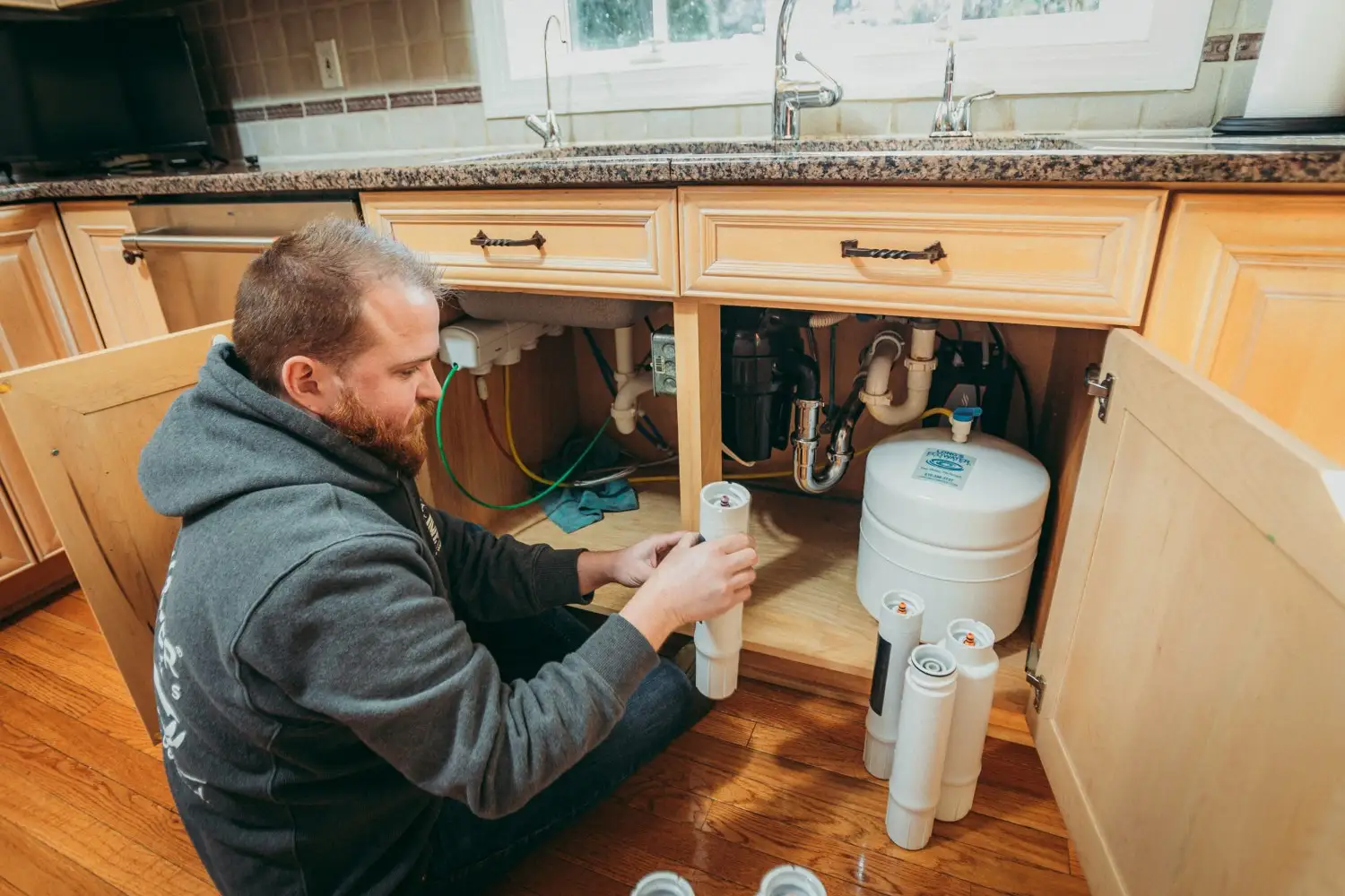 Man servicing under-sink water filter system.