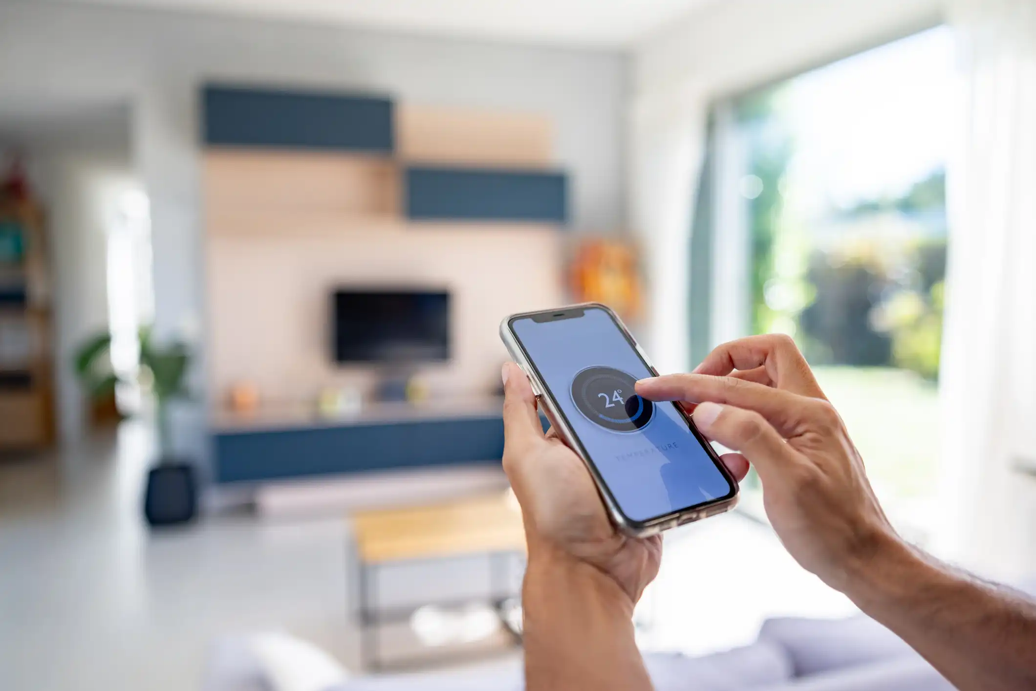 Hands adjusting a thermostat on a smartphone screen showing '$24^\circ$' C.