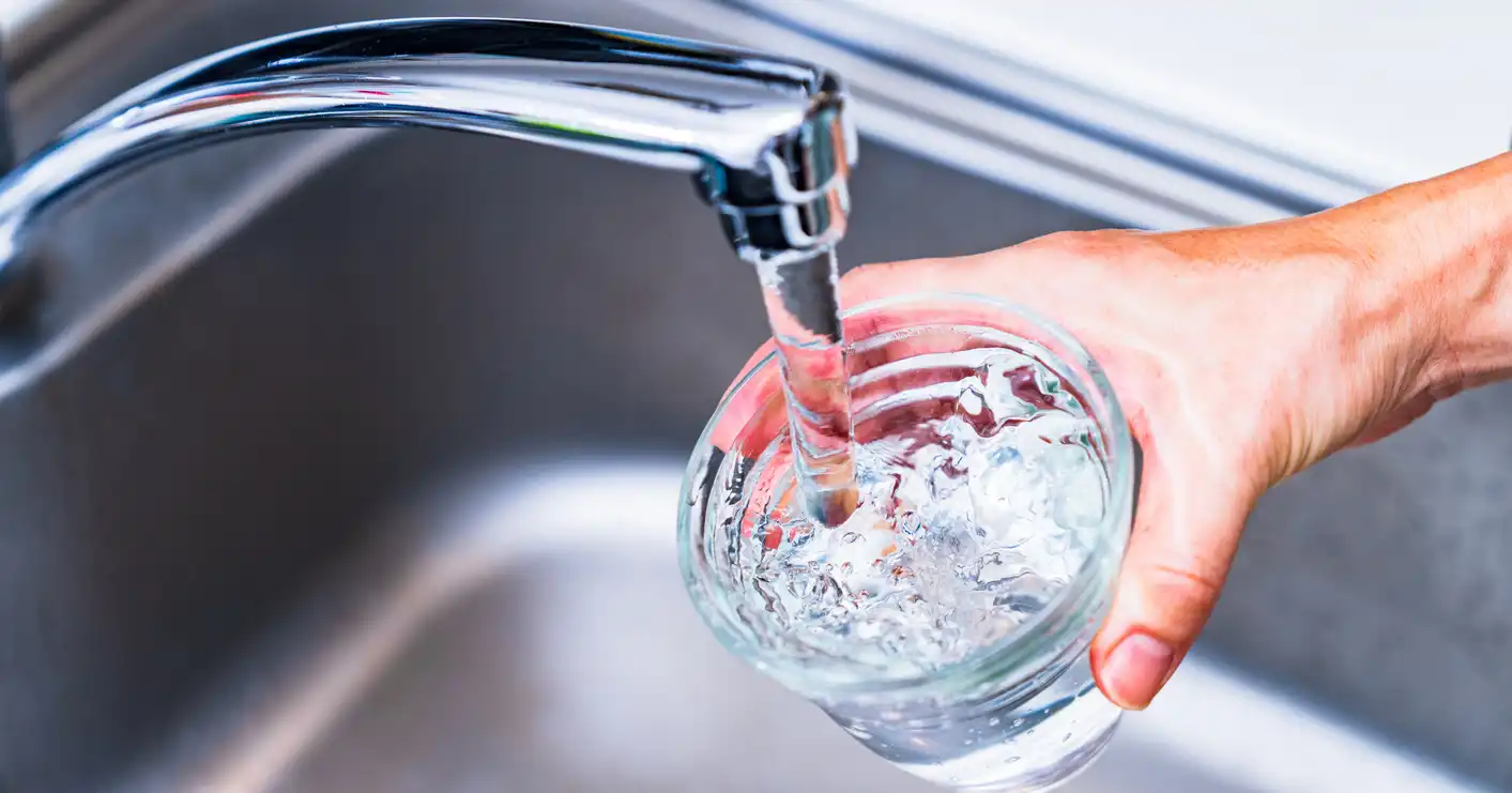 Hand filling a clear glass with running water from a modern kitchen faucet.