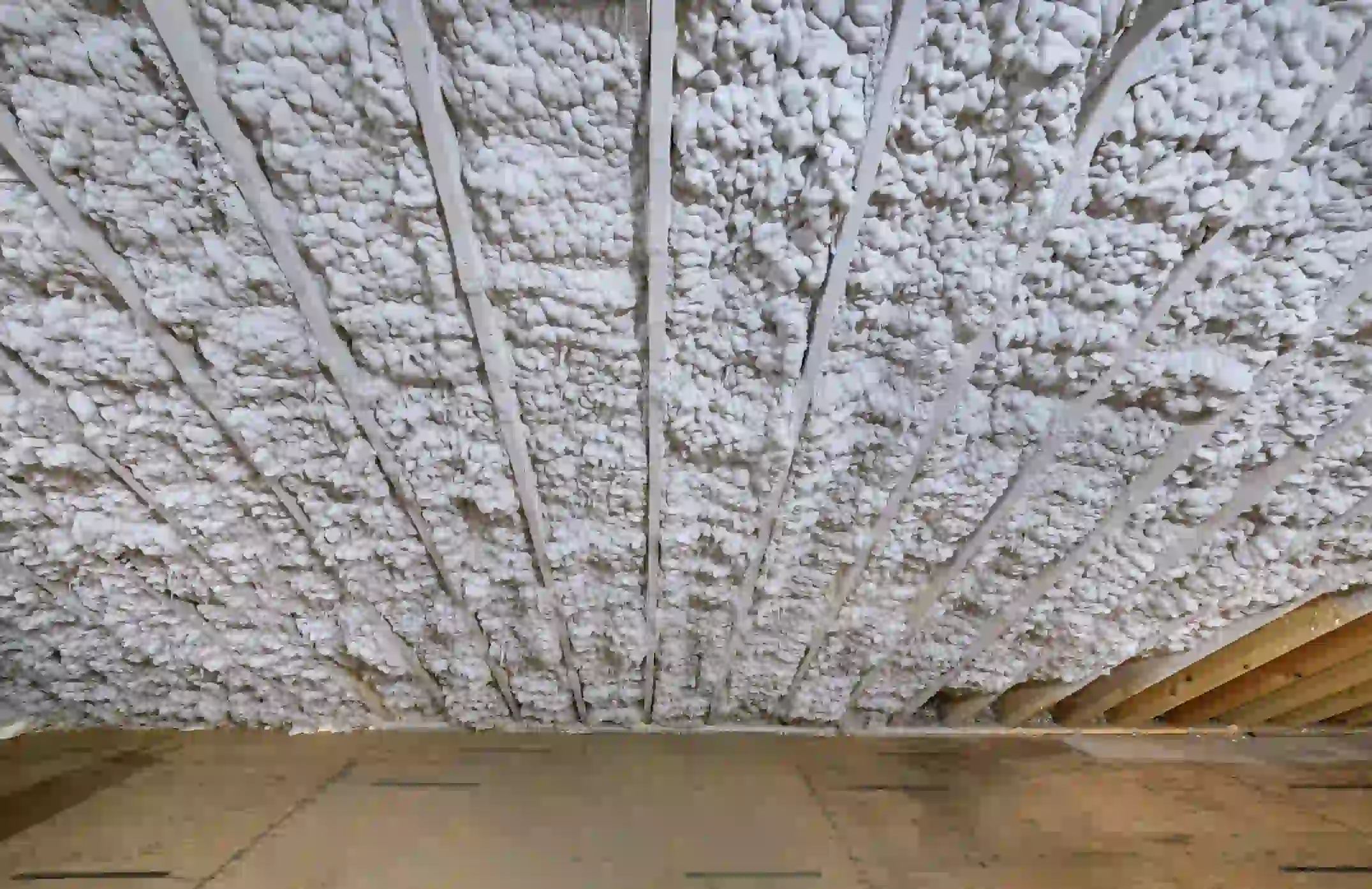 A wide-angle image, looking up at the underside of a roof or floor assembly, that has been insulated with a thick, textured layer of spray foam insulation.
