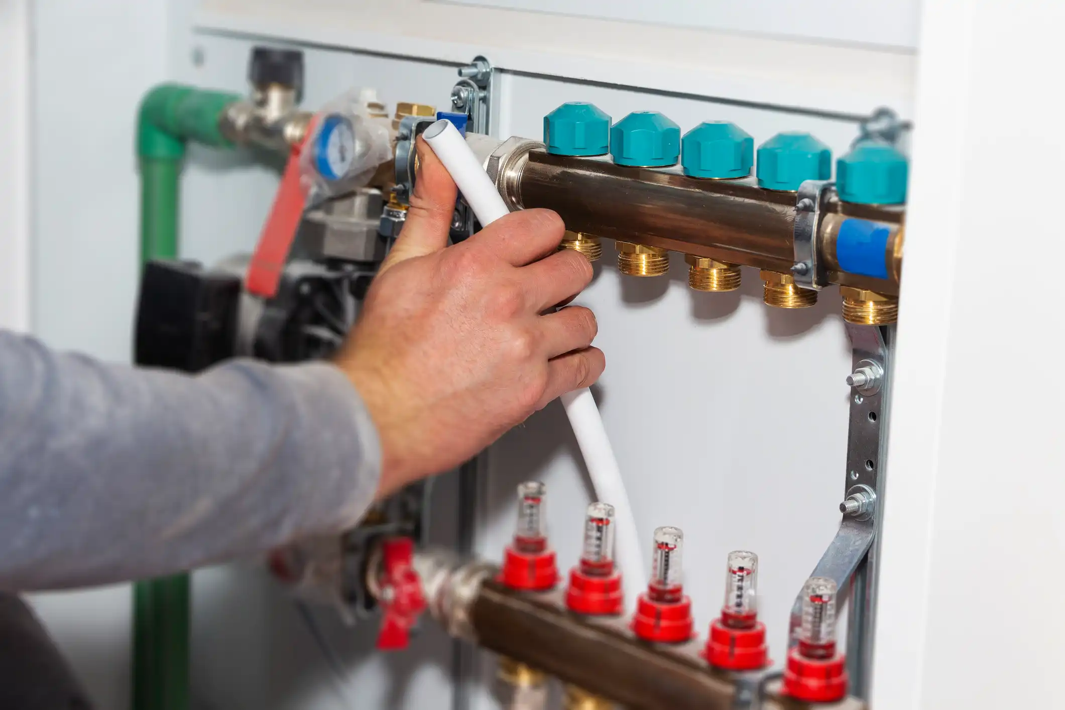 Hand connecting a white PEX pipe to a brass heating manifold.