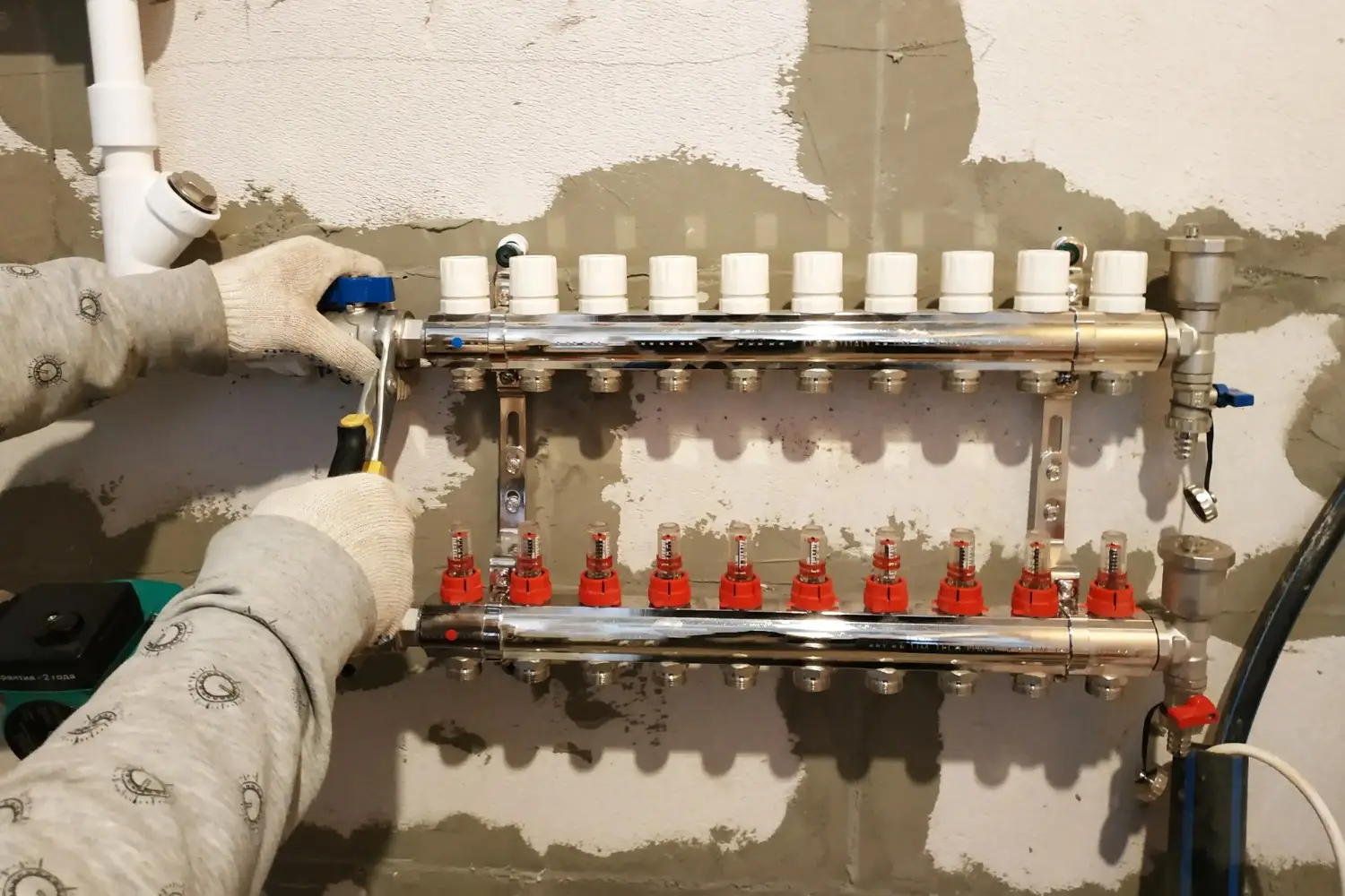 Worker adjusting a chrome underfloor heating manifold with gauges.