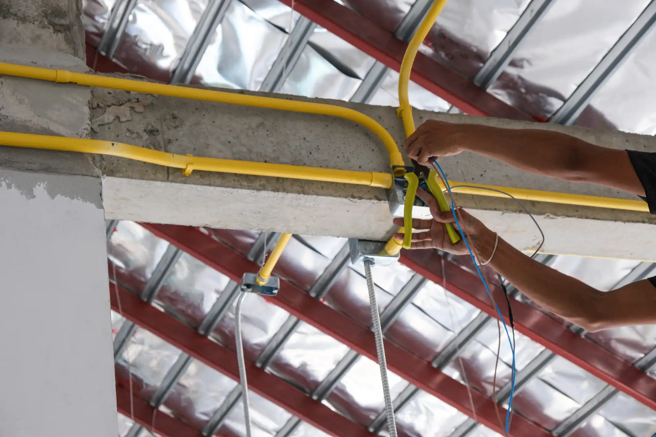 Construction worker running yellow electrical conduit in a ceiling.