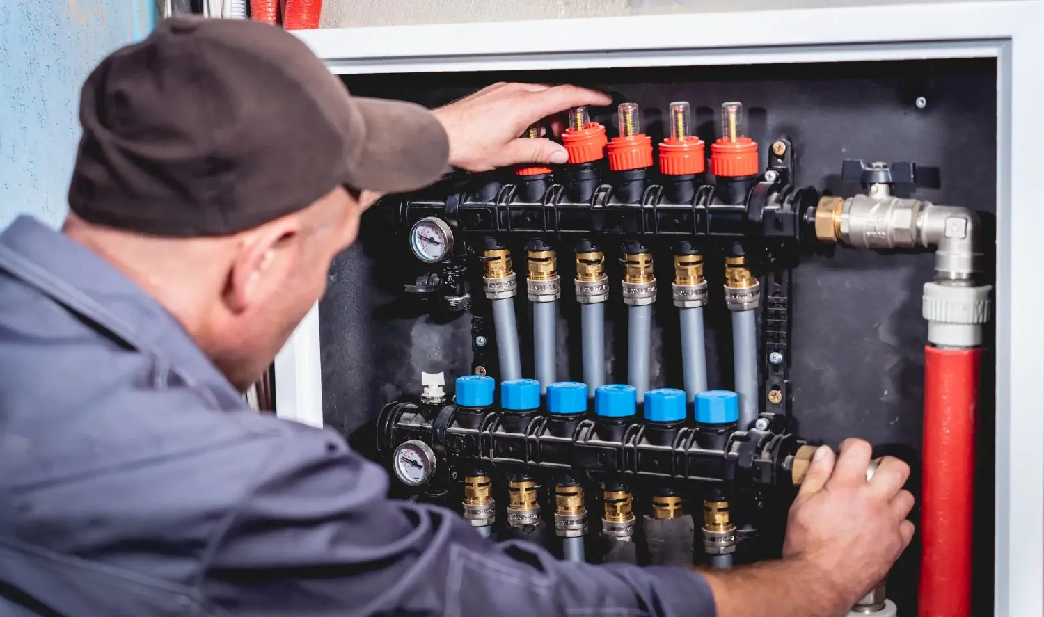 Worker adjusting a hydronic heating manifold with red and blue flow adjusters.