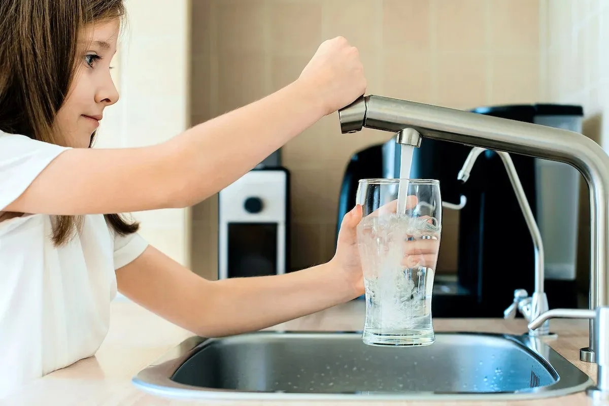 Girl filling glass from kitchen faucet.