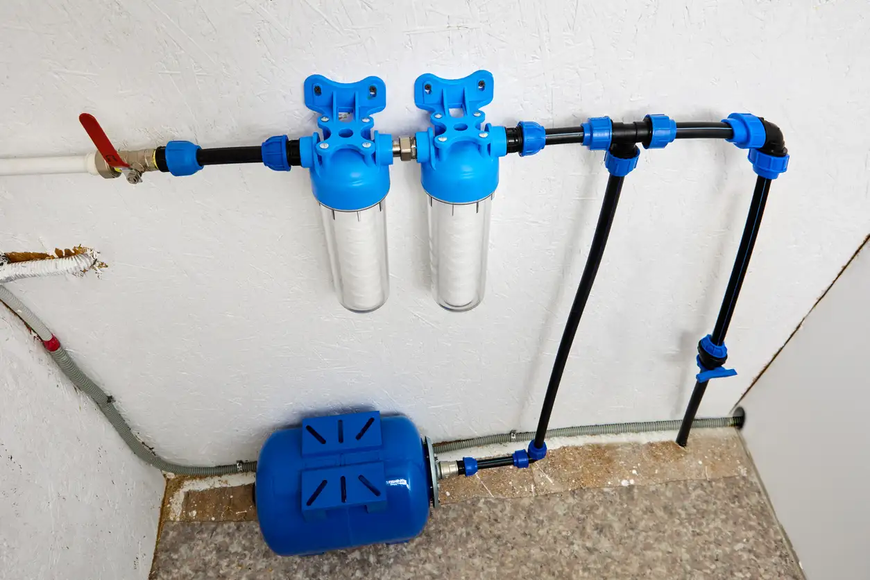 Two-stage sediment water filtration system mounted on a wall with blue housings and a pressure tank