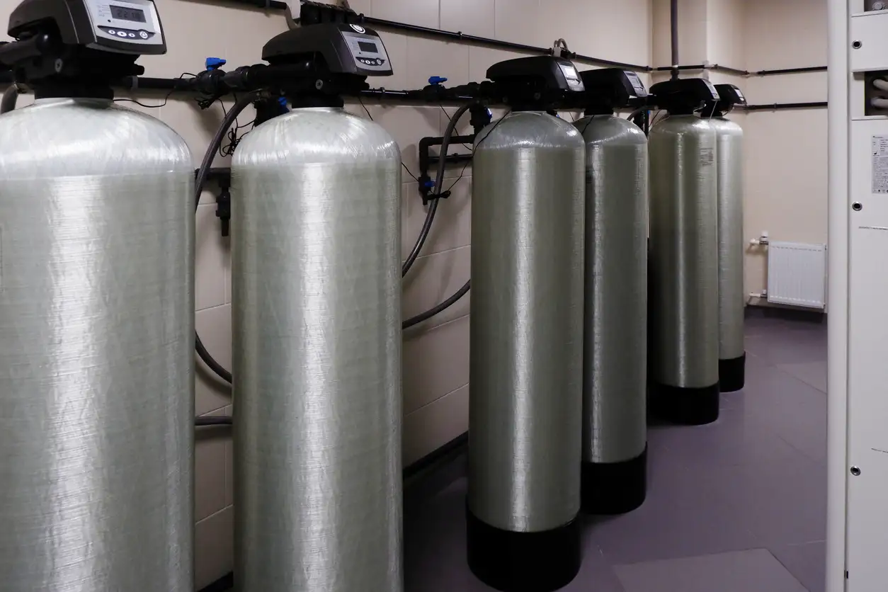 Row of large industrial-sized water softener tanks with digital control heads in a utility room