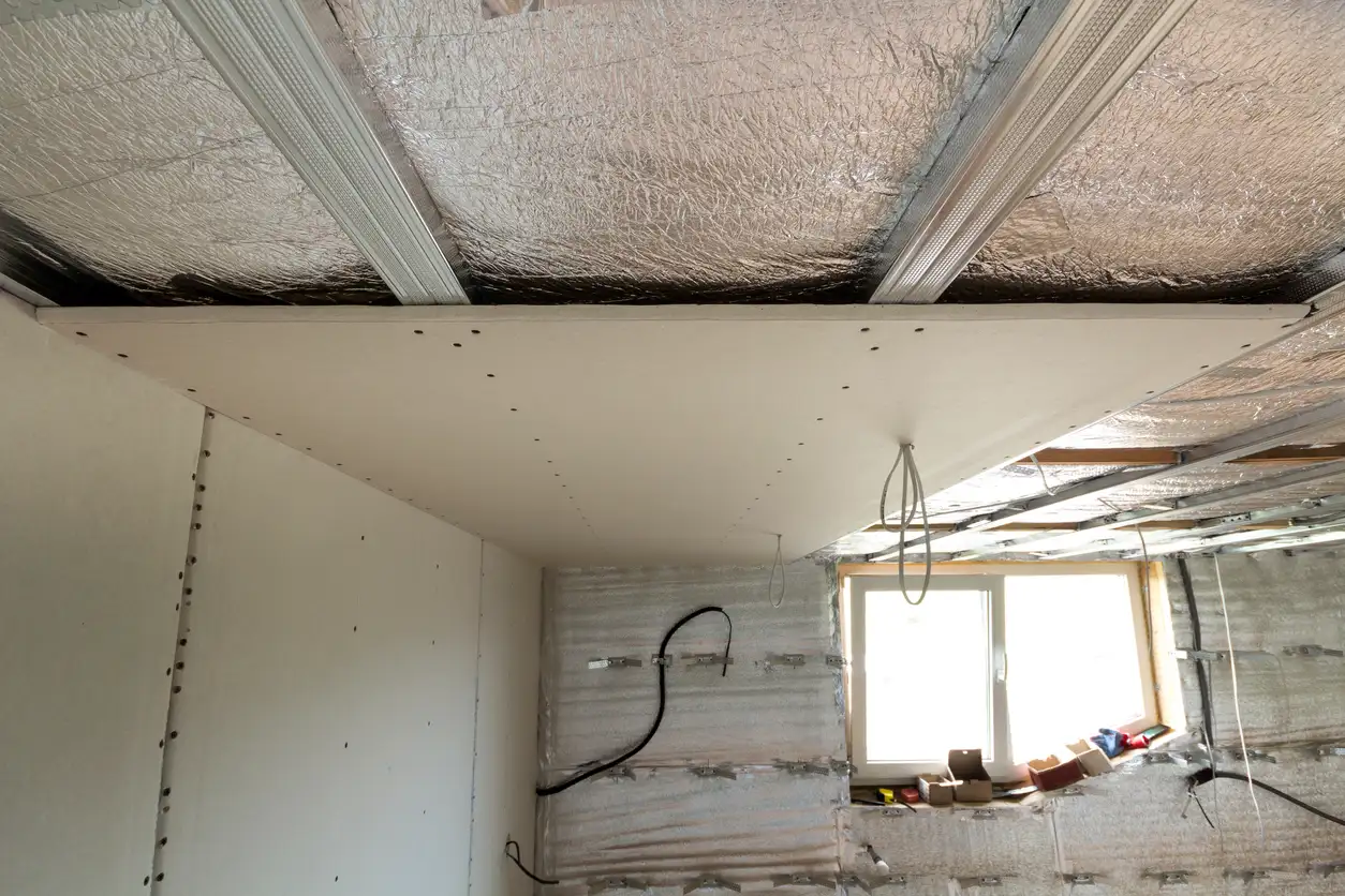 Interior construction site showing a newly installed drywall ceiling section against a silver radiant barrier
