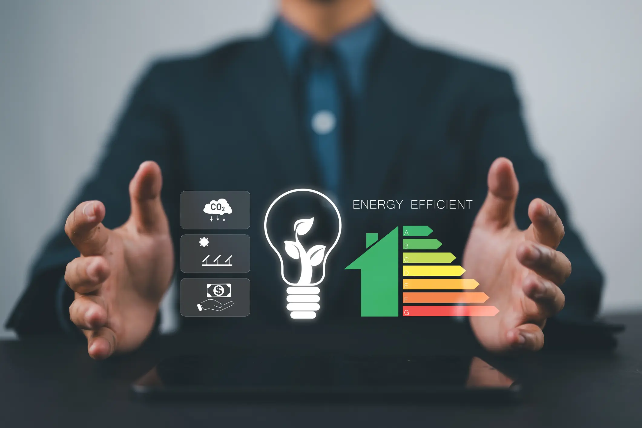 A person's hands are outstretched above a tablet, with a hologram of a lightbulb and house efficiency rating floating between them, surrounded by other icons related to energy and finance.