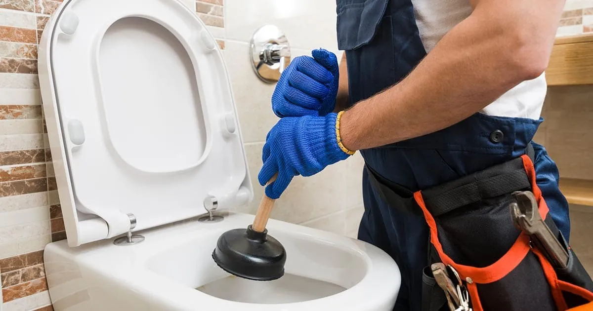 Plumber using plunger to unclog toilet.