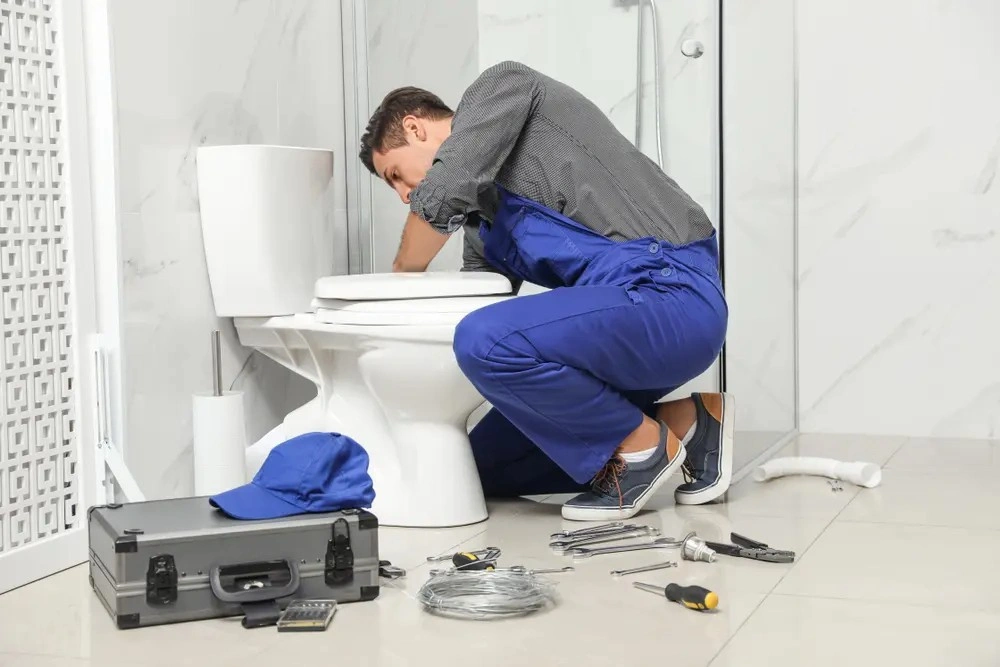 Plumber in overalls installing new toilet.