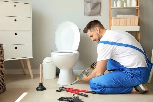 Plumber applying sealant to toilet base.