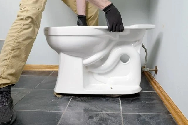 Gloved hands lifting white toilet bowl.