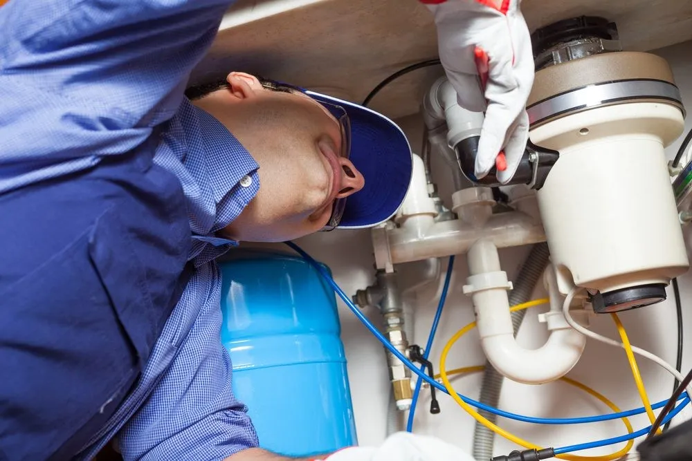Plumber in gloves repairing kitchen disposal.