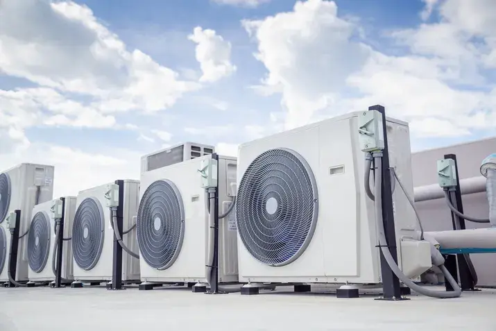 A row of white outdoor air conditioning units on a flat rooftop under a cloudy sky.