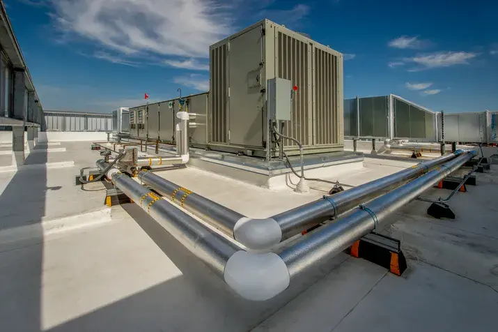 A large industrial HVAC unit on a rooftop with insulated silver pipes in the foreground.