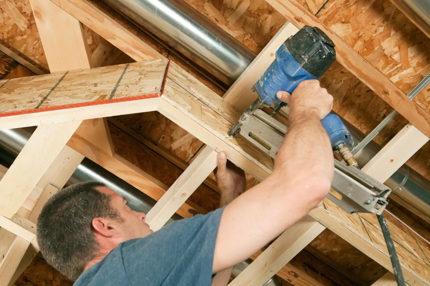 A worker using a nail gun to install wooden framing for crawl space air sealing.