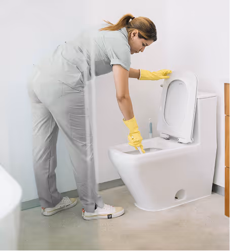 Woman wearing yellow gloves cleaning a white toilet bowl in a bathroom.