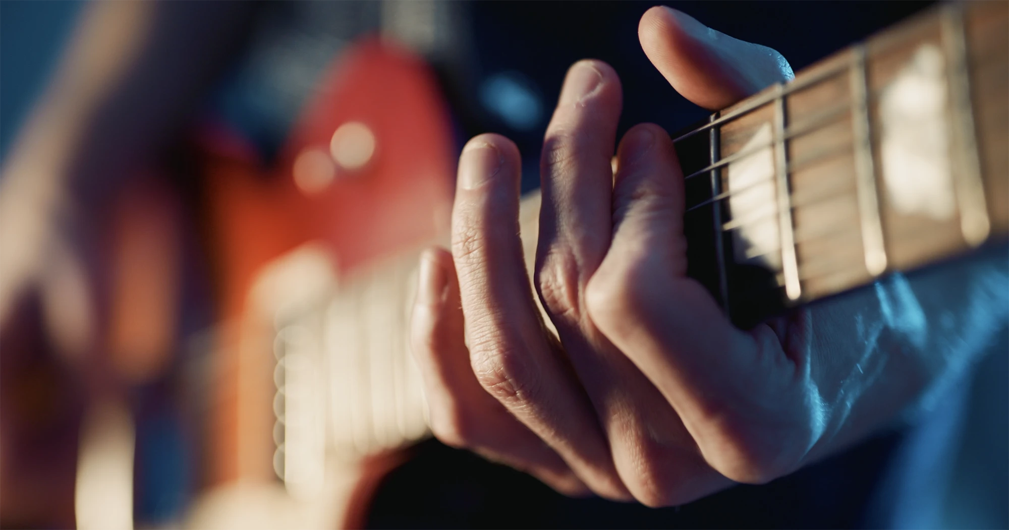 Close-up of fingers pressing guitar strings on the fretboard of a red electric guitar.