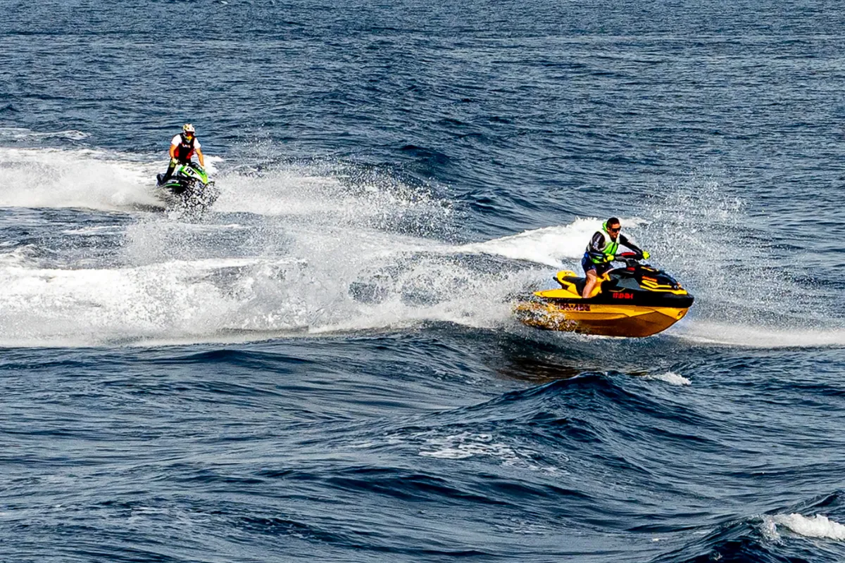 Two riders on jet skis crossing open water